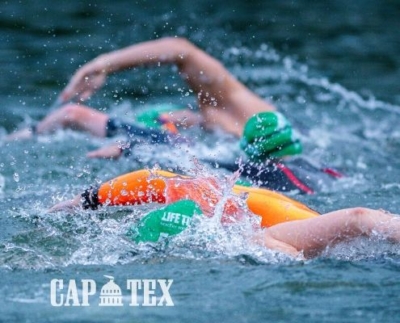 A focused triathlete in a wetsuit, goggles, and a swim cap powerfully swimming freestyle in open water, creating splashes with each stroke