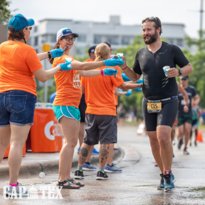 Man taking part in the run course portion of the Captex triathlon in Austin Texas takes cup of water from volunteer
