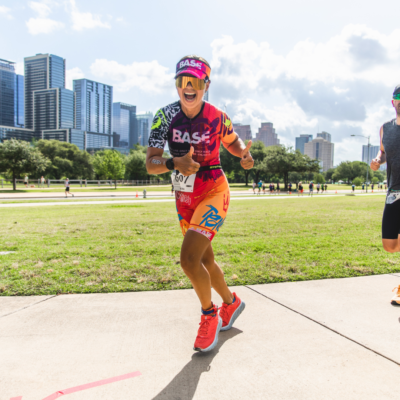 A woman running in the captor triathlon in Austin, Texas along a running trail in the bright sunshine with sunglasses gives the thumbs upA woman running in the captor triathlon in Austin, Texas along a running trail in the bright sunshine with sunglasses gives the thumbs up
